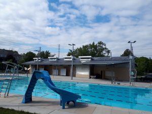 outdoor swimming pool with slide and large solar pool heating system on roof of facilities